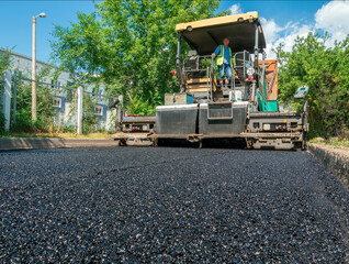 Fototapeta na wymiar A person is working at the road paver is laying an asphalt road in the city.