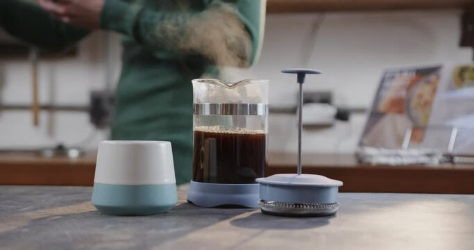 Midsection of caucasian man making coffee and using smartphone in kitchen, slow motion