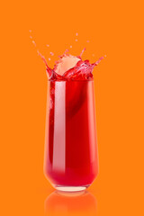 Berry red cold juice in glass with reflection, bright splashes, drops flying, swirl on orange background, copy space, vertical. Refreshing healthy summer beverage with splashing.