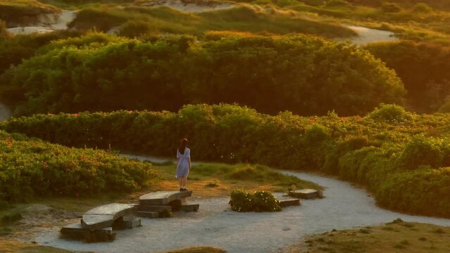Drone orbit around woman with arms out cinematic sunset light, dunes of Katwijk