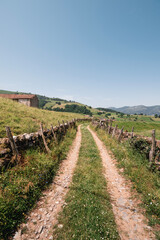 Obraz premium Rural track or road with stone walls and a farmhouse in the beautiful and green rural valley of Baztan on a sunny summer day in the north of Navarra, Euskal Herria