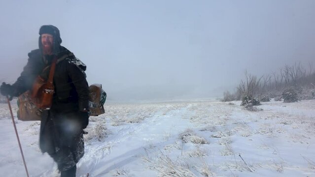 A man dressed as a polar explorer carries a swag in a snow storm blizzard through the mountains of Australia.
