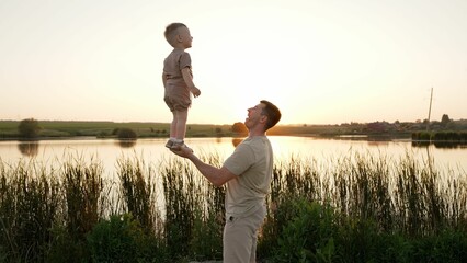 The trust of the son to the father. The father holds his son in full growth in the palm of his hand. Dad and son doing gymnastic exercises in nature. The father holds his son in one hand.