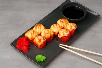 Baked sushi rolls on black plate on gray background