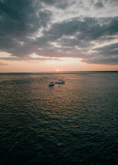 Boats floating in the sea under an overcast cloud on a sunset.