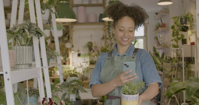 Young adult Female Retail Clerk Taking Picture with Phone of Plant in Store