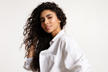 Beautiful smiling young modern woman with curly bouffant long hair wearing white oversize shirt on white background