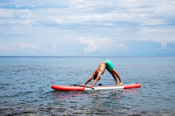 Yoga on the surf with a paddle. Adho mukha shvanasana on surf boards. A man does an asana dog face down