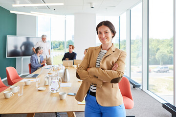 Portrait of smiling female professional wearing blazer standing with arms crossed against...