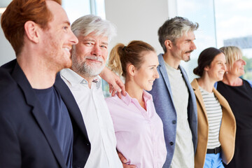 Portrait of smiling senior businessman standing with arms around colleagues at office