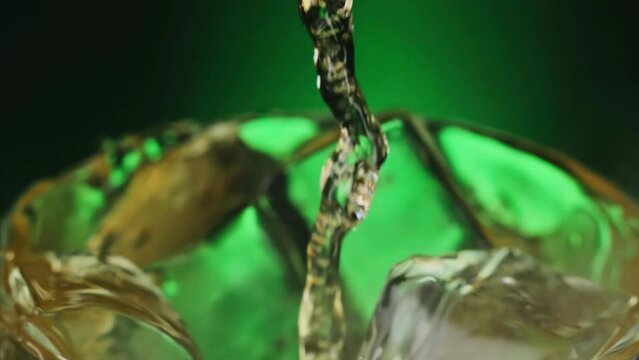 Slow motion 1000fps on pouring absinthe liquid on ice cubes in rotate glass. Super slow motion poured alcohol on spin ice cubes in turn glass. Slow motion pours green drink liquor on steam ice cubes