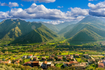 Obraz premium landscape of green summer highland mountain range with green beautiful valley with nice town below and amazing blue cloudy sky