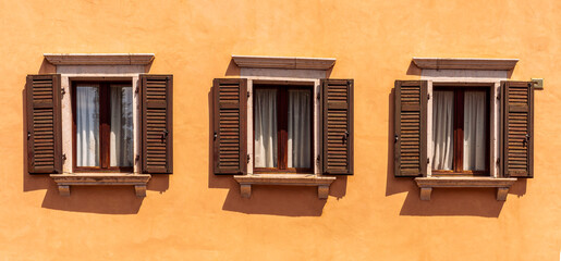 Fototapeta na wymiar old yellow facade of house with three brown vintage wooden windows in retro italian european style