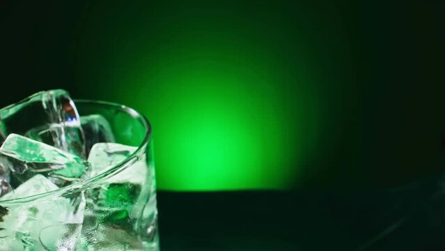 Slow motion 1000fps on pouring absinthe liquid on ice cubes in rotate glass. Slow motion pours green drink liquor on steam ice cubes.Super slow motion poured alcohol on spin ice cubes in turn glass