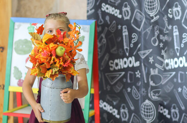 Banner with a little happy girl with a bright autumn bouquet of leaves in the classroom. The background is a school class. Back to school. Education concept.