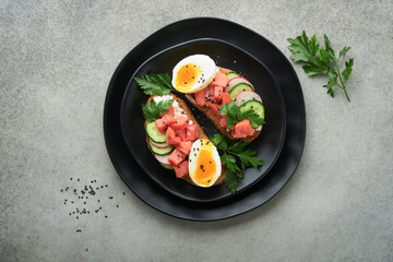 Healthy sandwich with bread or toast, smoked salmon, soft egg, cream cheese, cucumber, radish, black sesame and parsley on black plate. Delicious protein fish sandwich for breakfast. Smorrebrod.