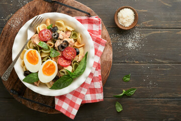 Italian pasta salad. Orecchiette pasta with tuna, tomato cherry, olive, basil and parmesan cheese in plate on dark wooden old rustic table background. Traditional Italian cuisine. Flat lay. Copy space