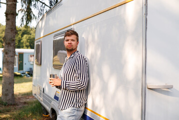 Portrait of a man in a striped shirt, holding a cup, standing near a mobile home outdoors