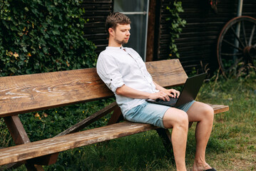 Fototapeta premium Portrait of a handsome man working with laptop sitting on a bench