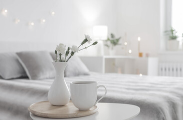 Fototapeta na wymiar cup of coffee and white flowers in vase on table in bedroom