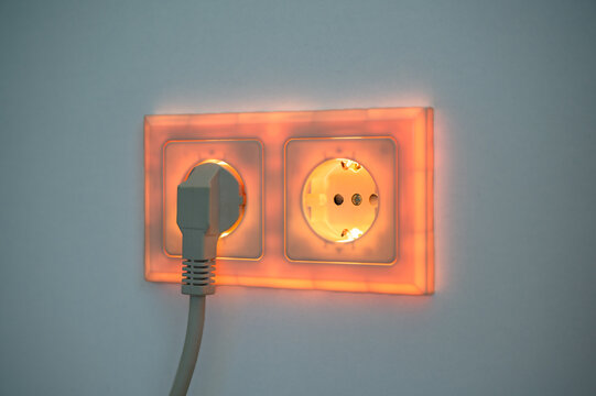 Yelow illuminated socket with plug inserted to symbolise power consumption and electrical energy from a socket outlet