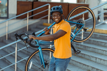 Portrait of handsome smiling African American man wearing helmet holding his bicycle walking on...