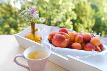 Naklejka na ściany i meble on wooden white tray plate with orange apricots, peach, bunch wild flowers on table in garden, beautiful summer still life, fruits, green trees in background, concept picnic in nature, healthy eating
