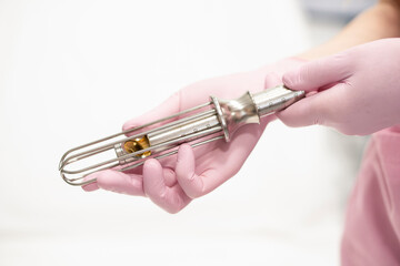 Close-up of the hands of a female doctor gynecologist in pink medical gloves, holding metal tools,...