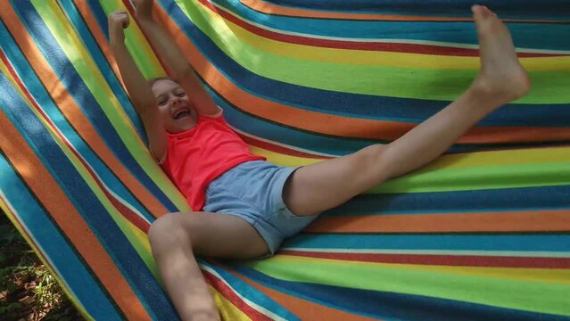 Happy little girl in a hammock laughing and having fun in outdoors. Sunny summer day