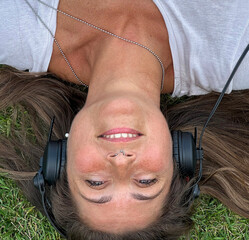 Young woman lying down on grass wearing stereo headphones listening music.
