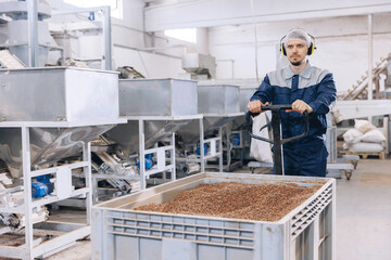 Man loader in uniform working trolley with cedar nuts pine in warehouse. Industrial manufacturing...