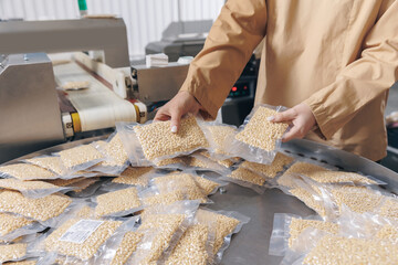 Young woman production worker stands behind automatic conveyor belt for transporting vacuum packed cedar nuts. Concept food industry plant
