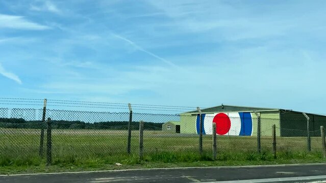 Driving past Royal Air Force, RAF airfield and some building behind wired fence, car side window view.