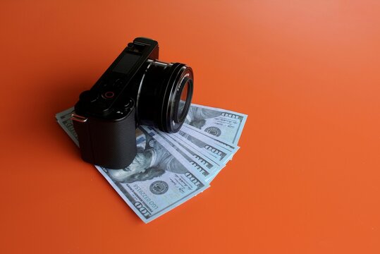 Mirrorless camera and money on orange background with copy space. Profitable photography business and expenses concept