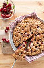 Cake with cherries and almonds on light wooden table