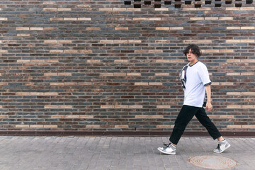 Fototapeta na wymiar young man walks down the street in front of a brick wall