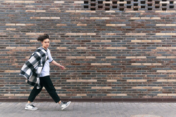 young man walks down the street in front of a brick wall