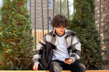 young man typing something on the phone while sitting in the park