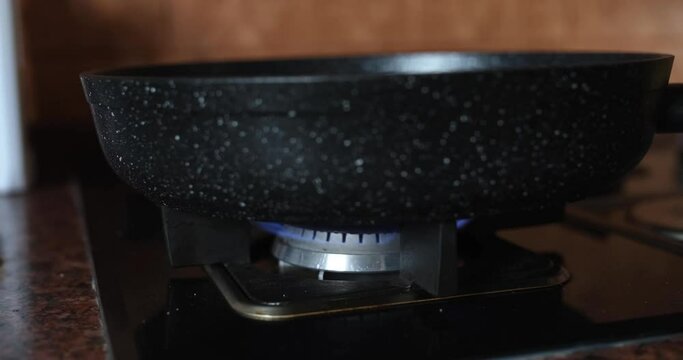 Ceramic black frying pan on a burning gas burner. Safe cooking utensils, built-in modern gas stove