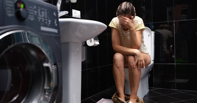 A woman is crying while sitting on the toilet in the bathroom at home. Abdominal pain, diarrhea