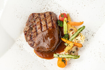 Grilled beef tenderloin with Demi glace sauce with grilled vegetables on a white porcelain plate