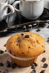 Muffin or cupcake with chocolate chips on wooden table background. Concept of making industrial or homemade pastries.