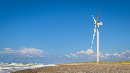 Windrad steht an der Küste in den Dünen am Strand und erzeugt alternative Energie durch Wind
