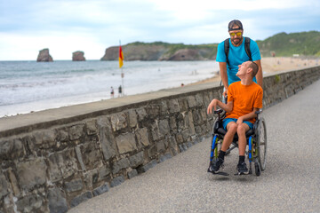 A disabled person in a wheelchair being pushed by a friend by the beach, having fun in summer