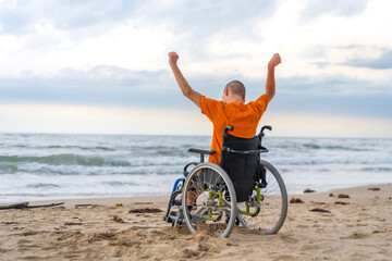 Fototapeta premium Disabled person on his back in a wheelchair on the beach with open arms enjoying the freedom