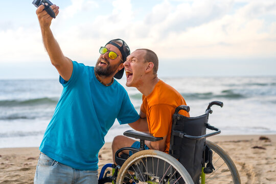 A disabled person in a wheelchair on the beach having fun with a friend and a video camera, taking a selfie