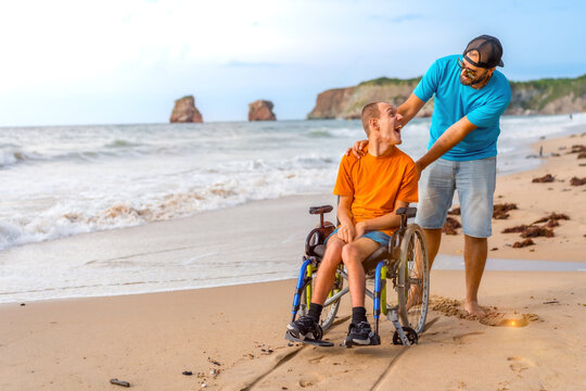 A disabled person in a wheelchair on the beach pushed by a friends by the sea
