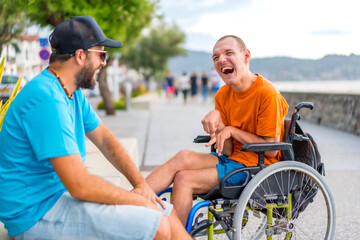 A disabled person in a wheelchair with a friend on summer vacation having fun laughing a lot by the...