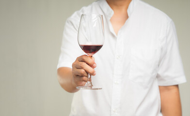 Close-up of hand holding a glass of red wine while standing on a gray background.