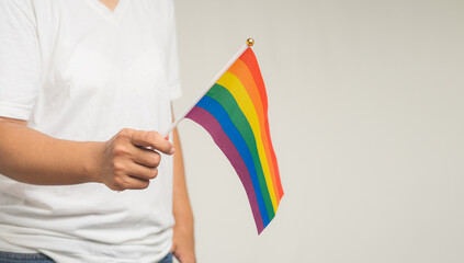 Close-up of a hand holding a rainbow flag while standing on a gray background.